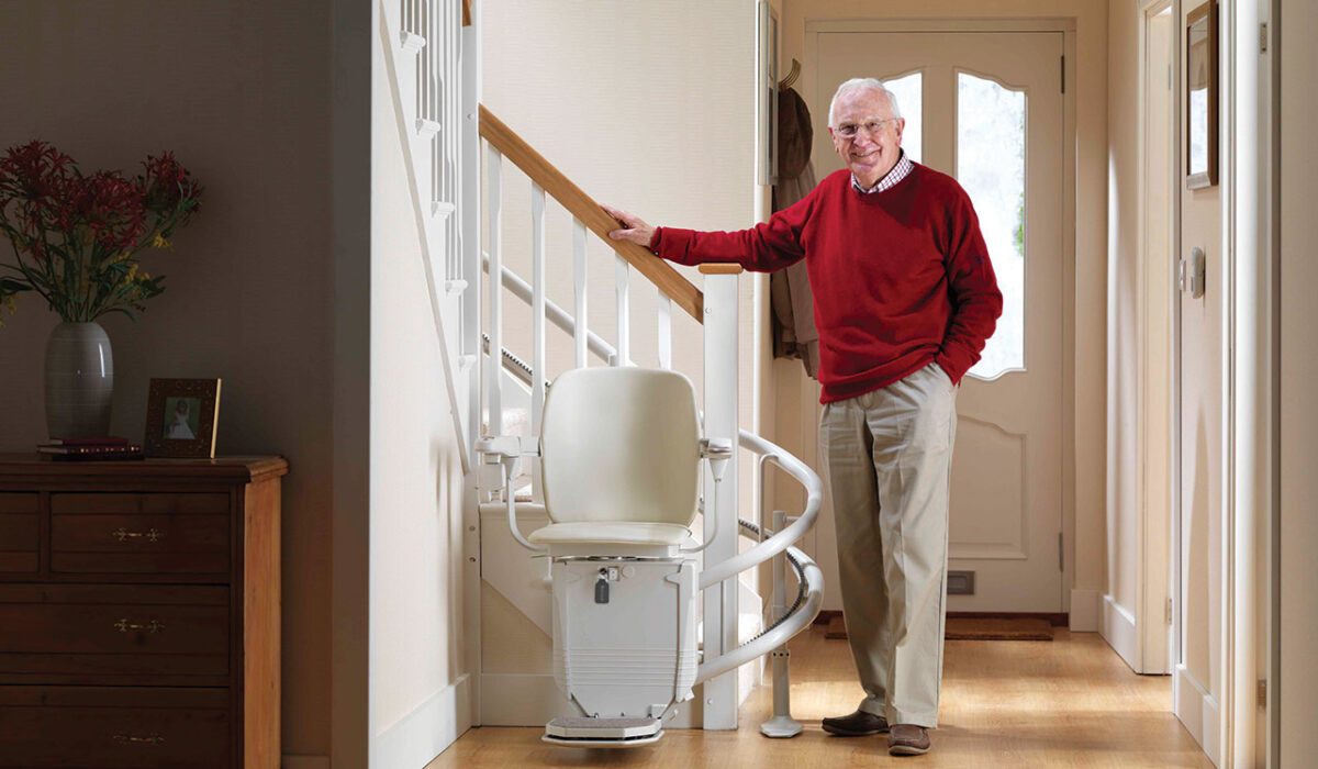 Man in red sweater standing next to curved stair lift